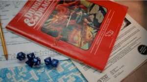 A vintage Dungeons & Dragons red box set, blue dice, character sheet, and pencil on a tabletop, with a map partially visible underneath.