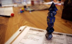 A stack of blue polyhedral dice on top of a Dungeons & Dragons character sheet displaying combat details.