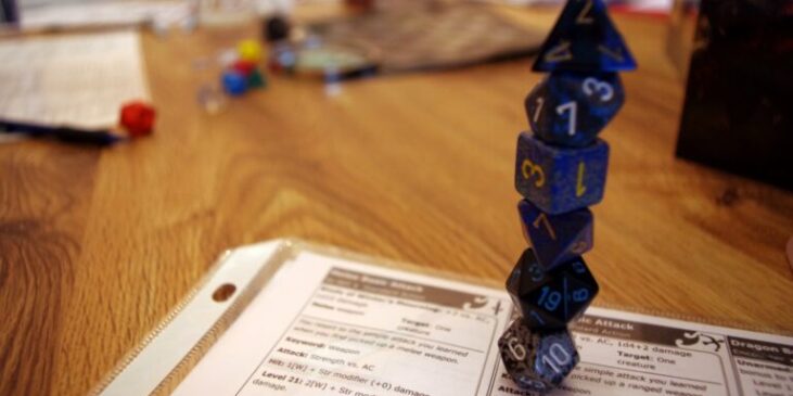 A stack of blue polyhedral dice on top of a Dungeons & Dragons character sheet displaying combat details.